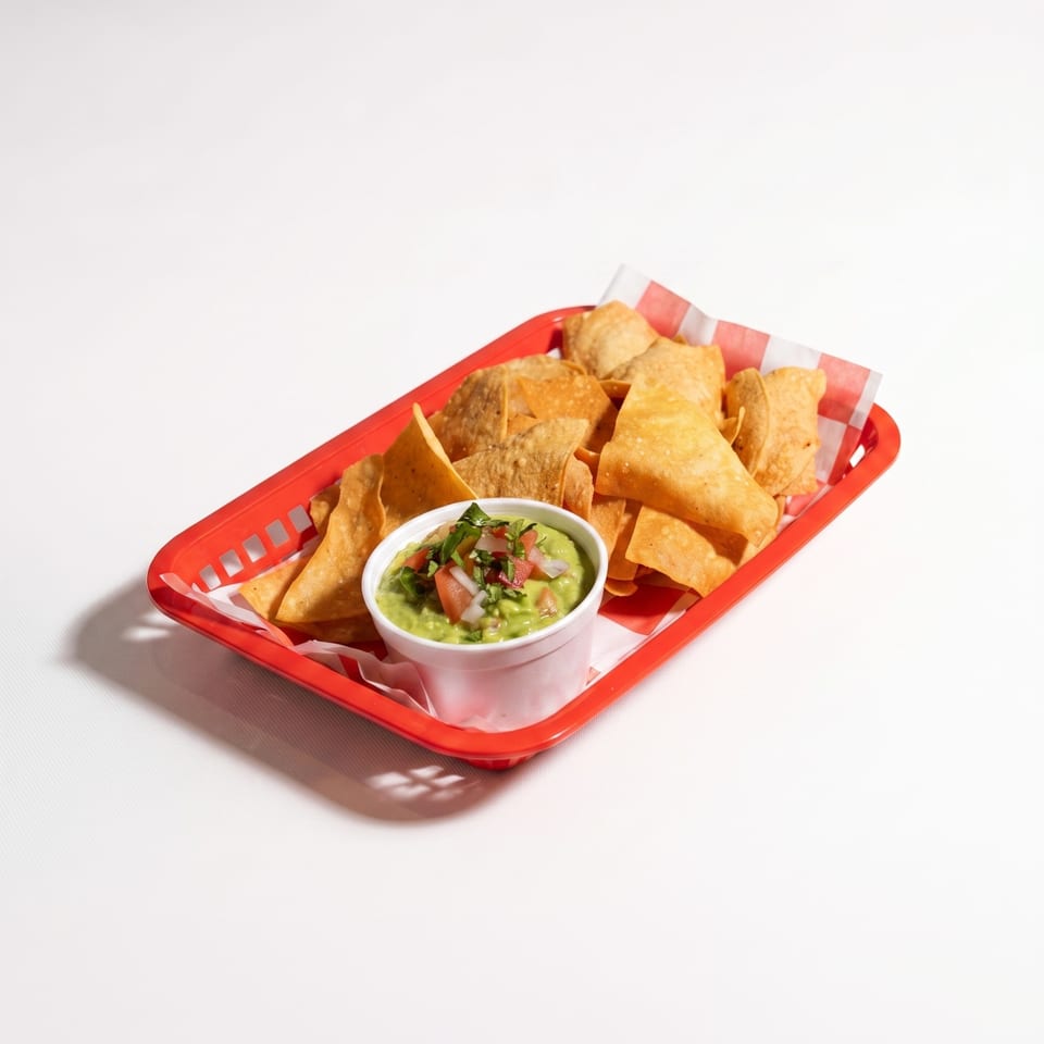 Red basket filled with tortilla chips and crispy tacos, served with guacamole topped with pico de gallo.